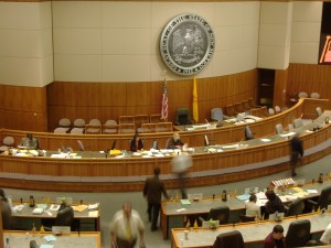 Interior view of NM State Senate chamber platform, with State Seal on the wall behind.