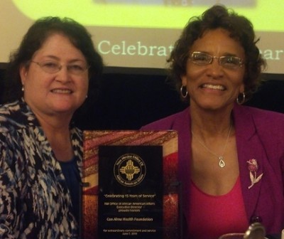 Con Alma Executive Director Dolores E. Roybal and former Board of Trustees Chair Pamelya Herndon display the award plaque.
